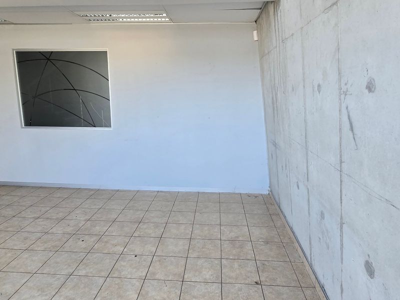 An empty industrial office space featuring an exposed concrete feature wall, tiled flooring, and a suspended ceiling with recessed lighting.