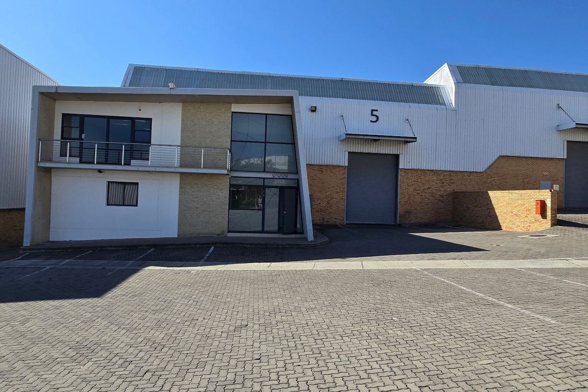 Front elevation of an industrial warehouse complex featuring roller shutter doors, paved parking area, and a multi-level office component with a balcony.