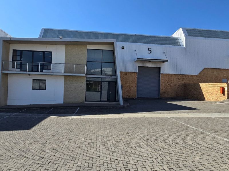 Front elevation of an industrial warehouse complex featuring roller shutter doors, paved parking area, and a multi-level office component with a balcony.