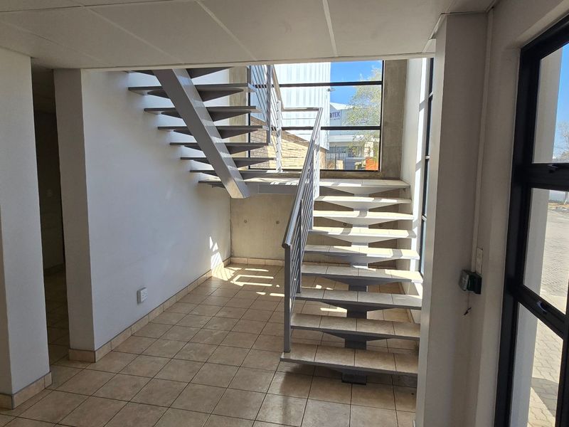 Bright industrial entrance foyer featuring a modern metal staircase, tiled flooring, and large windows providing ample natural light.