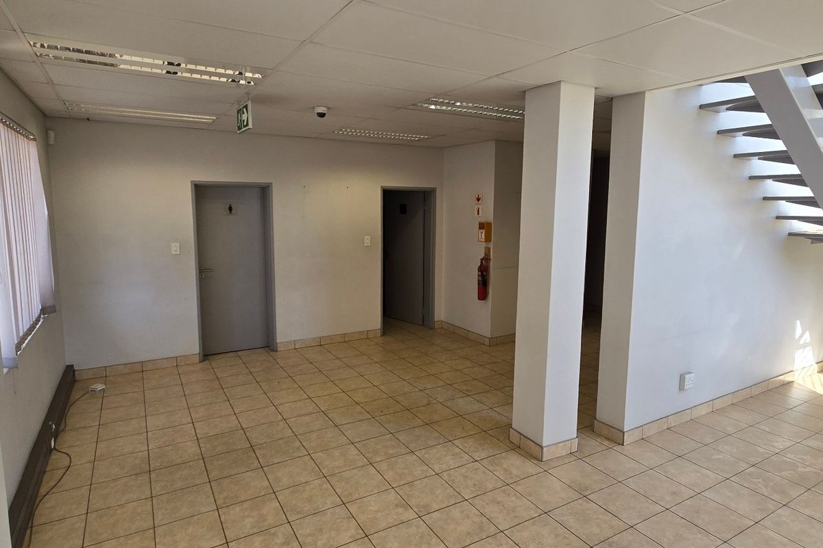 An open-plan industrial hallway featuring ceramic tile flooring, a metal staircase, and functional recessed lighting, providing access to multiple internal rooms.
