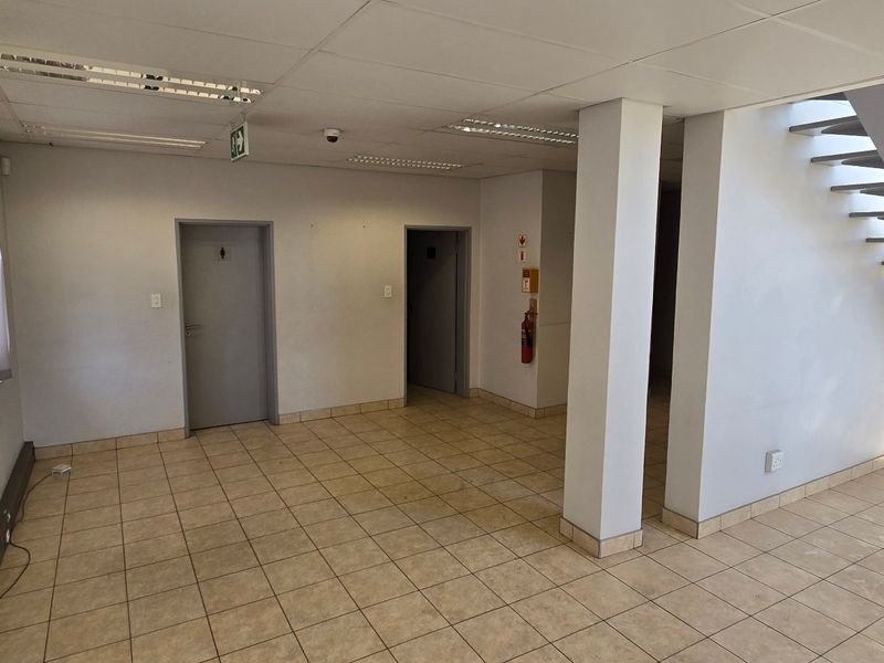 An open-plan industrial hallway featuring ceramic tile flooring, a metal staircase, and functional recessed lighting, providing access to multiple internal rooms.