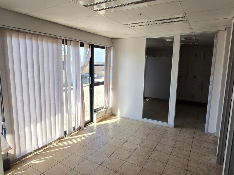 Empty office space featuring tiled flooring, suspended ceiling with recessed lighting, and glass partition walls, offering a clean and professional industrial workspace.