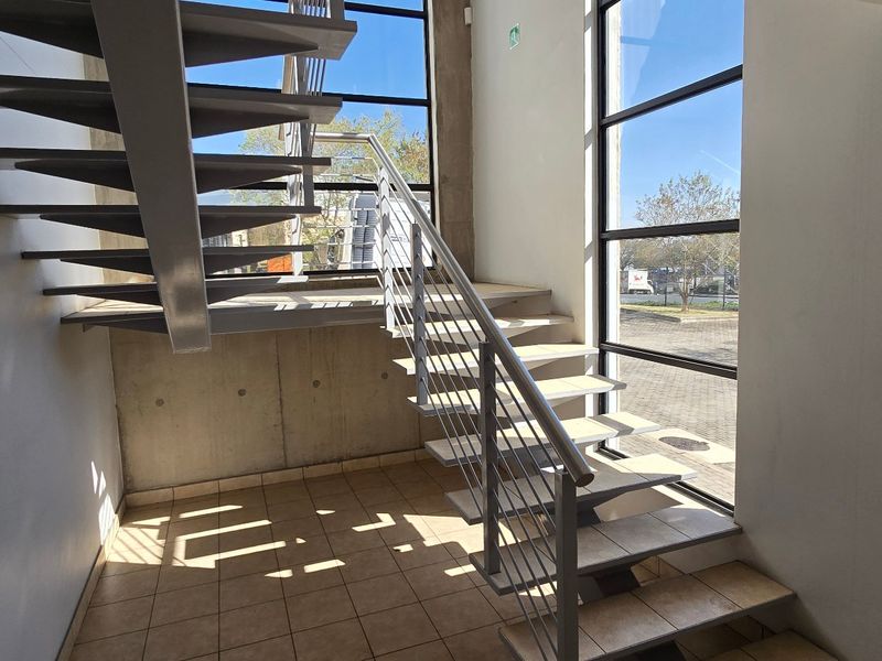 Modern industrial entrance featuring an open-tread staircase, exposed concrete wall, and expansive full-height windows providing ample natural light.