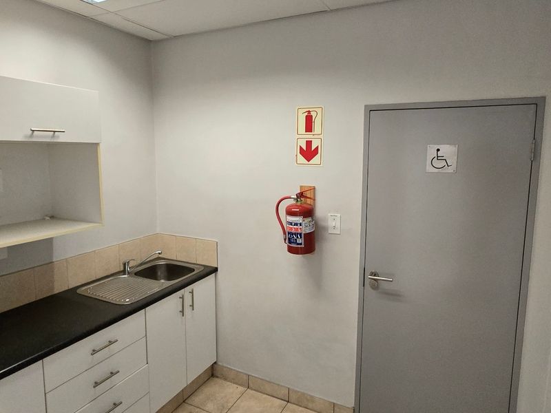 A functional kitchenette area featuring built-in cabinetry, a stainless steel sink, and an adjacent accessible doorway with safety equipment installed.