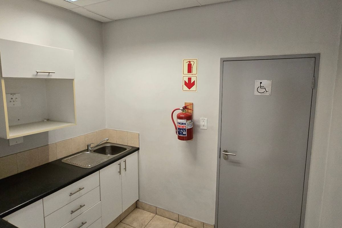 A functional kitchenette area featuring built-in cabinetry, a stainless steel sink, and an adjacent accessible doorway with safety equipment installed.