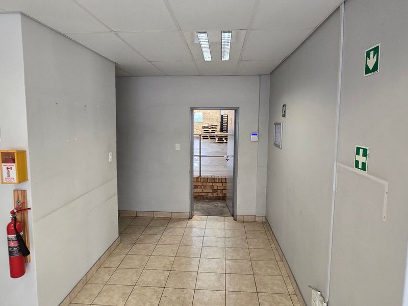 A clean, functional industrial hallway featuring tiled flooring, suspended ceiling with integrated lighting, and essential safety equipment including a fire extinguisher.