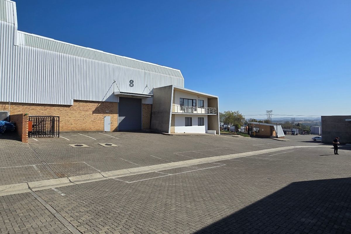 Industrial warehouse facility featuring a large paved yard, roller shutter access, and an attached office component with a balcony.