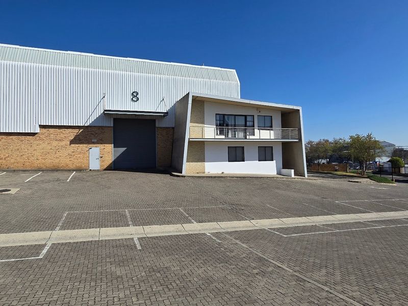 Industrial warehouse unit featuring a large roller shutter door, paved parking area, and a modern office section with a balcony.