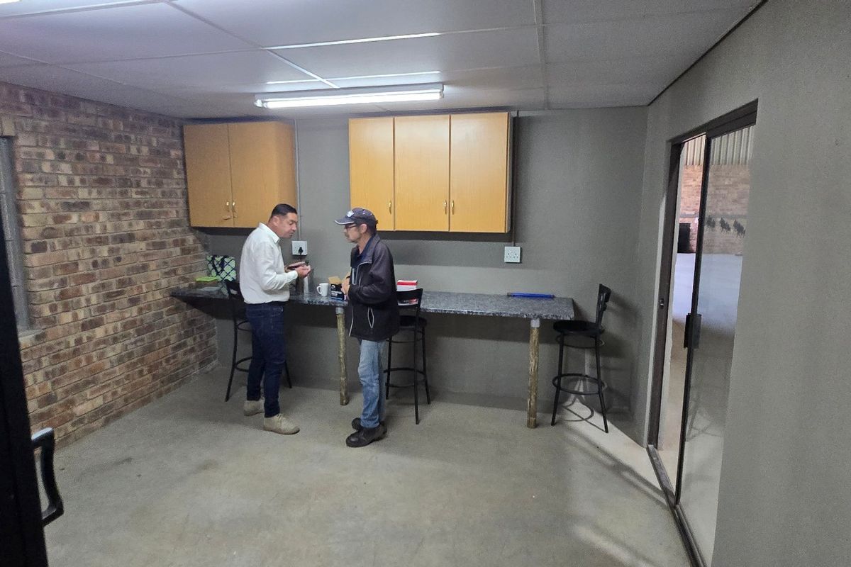 A functional kitchenette area featuring built-in cabinetry, a laminate countertop, and exposed brick wall detailing, suitable for office or industrial breakroom use.