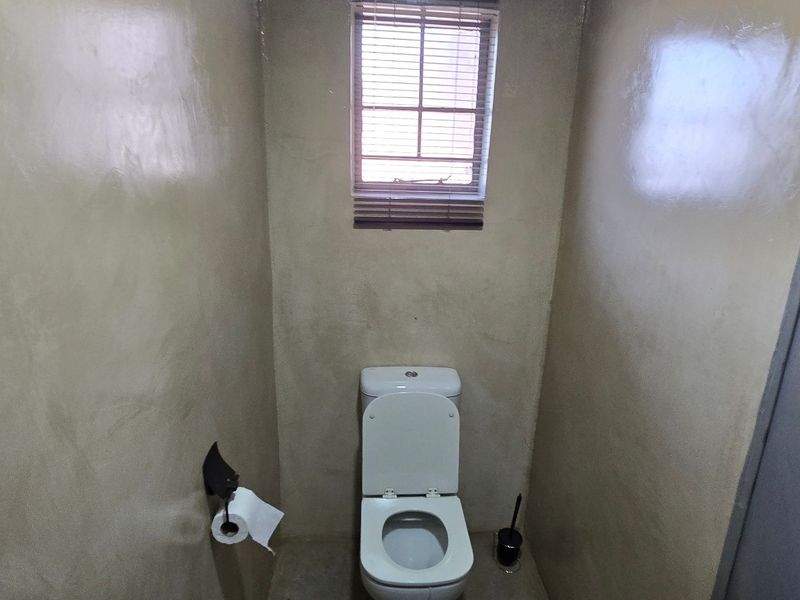 A compact bathroom featuring a standard toilet, smooth wall finishes, and a small window providing natural light.