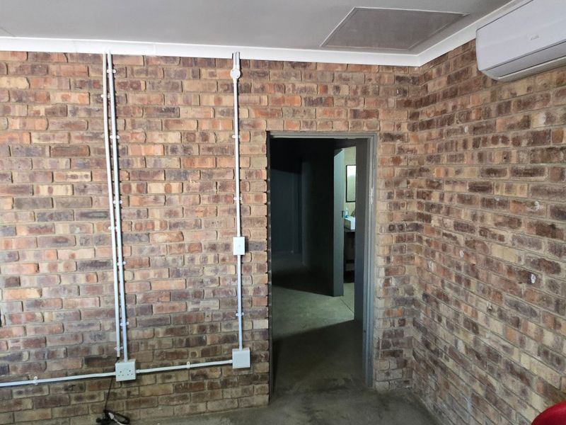 Industrial-style office space featuring exposed brick walls, surface-mounted electrical conduits, and a wall-mounted air conditioning unit.
