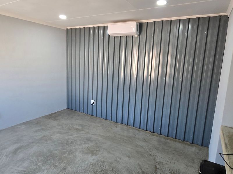 A clean, industrial-style utility space featuring polished concrete floors, corrugated metal wall cladding, and a wall-mounted air conditioning unit.