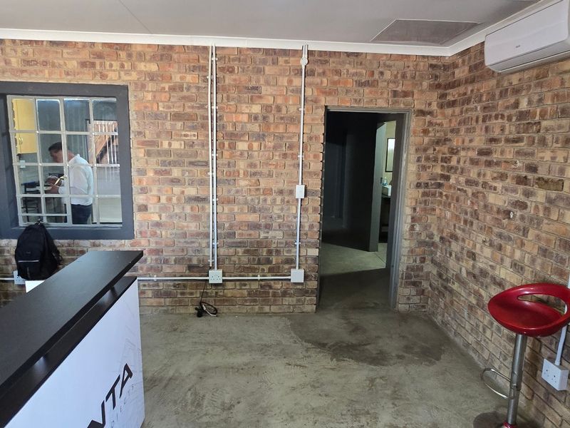 Industrial style office space featuring exposed brick walls, concrete flooring, and surface-mounted electrical conduits with an integrated air conditioning unit.