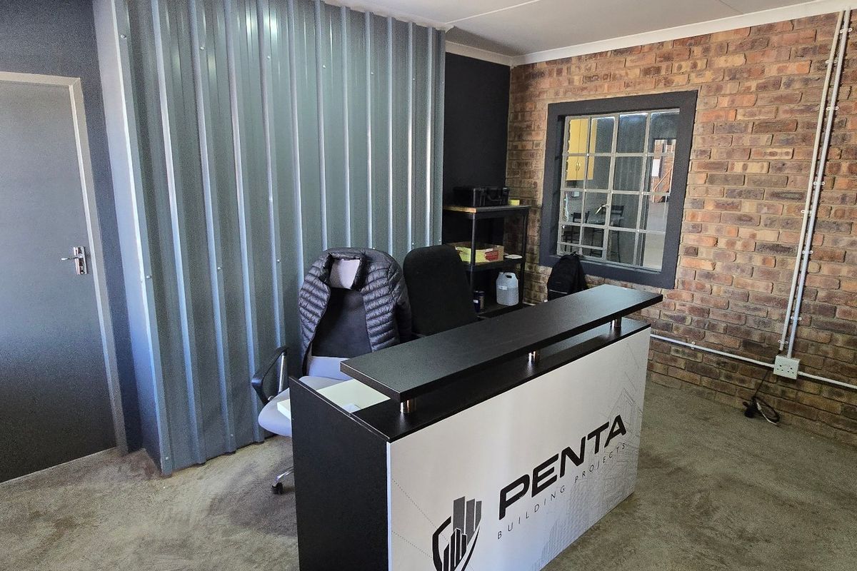 Industrial-style office space featuring exposed brickwork, corrugated metal partitioning, and concrete flooring, providing a functional and modern workspace environment.