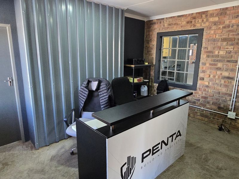 Industrial-style office space featuring exposed brickwork, corrugated metal partitioning, and concrete flooring, providing a functional and modern workspace environment.