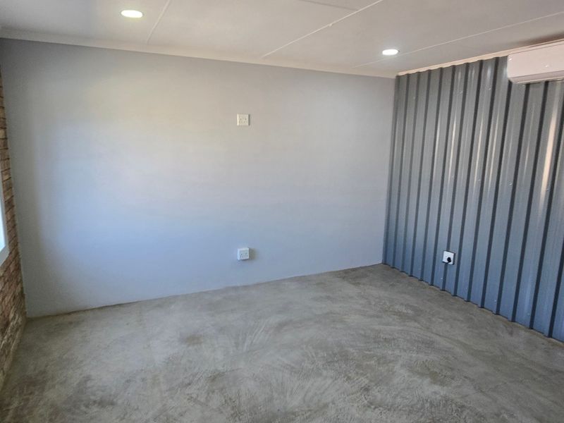 A clean, empty office space featuring exposed brickwork, corrugated metal wall cladding, polished concrete floors, and a wall-mounted air conditioning unit.