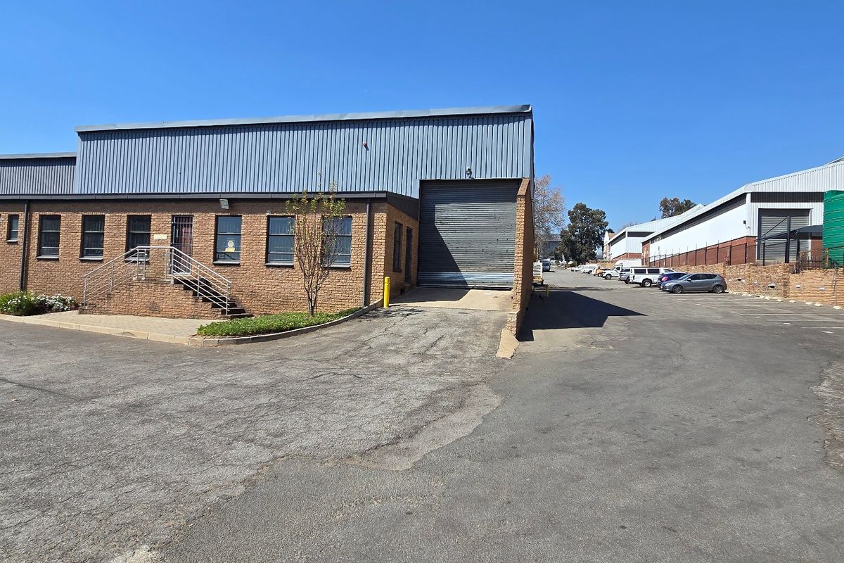 Industrial property exterior featuring a brick facade, roller shutter door, and paved driveway with adjacent water storage tanks.