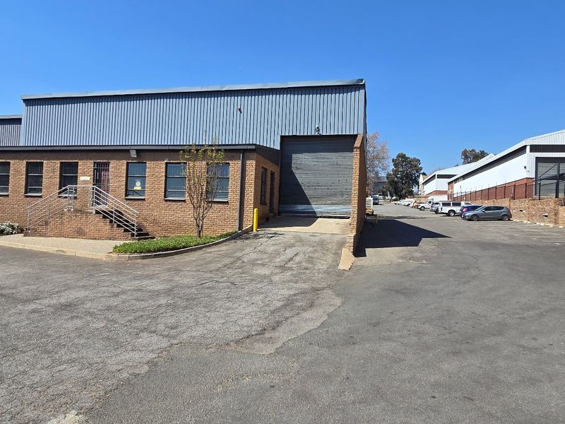 Industrial property exterior featuring a brick facade, roller shutter door, and paved driveway with adjacent water storage tanks.