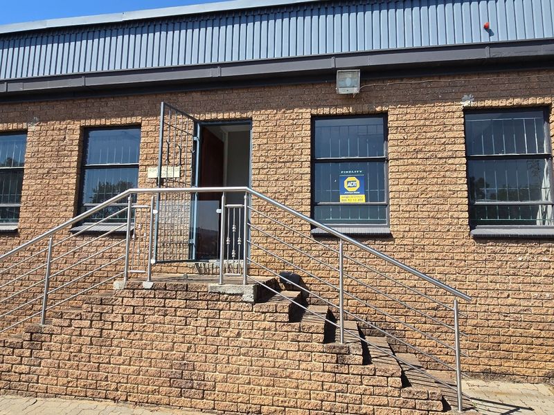 Front exterior view of an industrial building featuring a brick facade, stainless steel handrails, and a secure entrance staircase.
