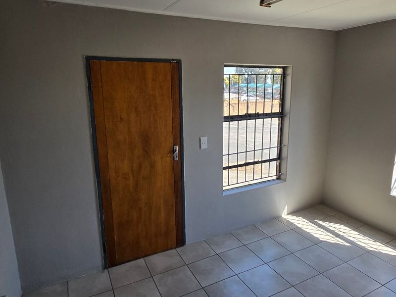 A clean, empty office space featuring tiled flooring, security bars on the windows, and a solid timber door.