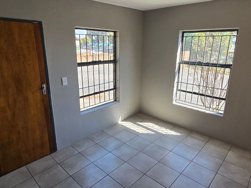 A clean, empty office space featuring tiled flooring, neutral walls, and windows fitted with security bars.