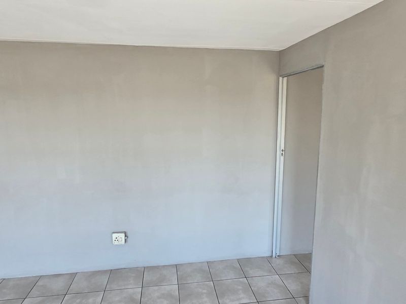An empty interior space featuring tiled flooring and freshly painted grey walls with two doorways.