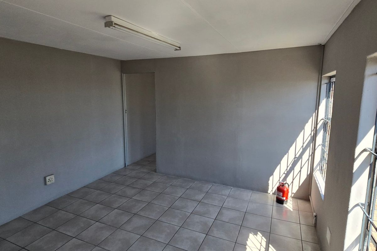 A clean, empty office space featuring neutral grey walls, tiled flooring, and large windows fitted with security bars.