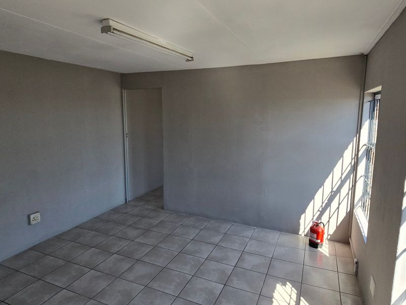 A clean, empty office space featuring neutral grey walls, tiled flooring, and large windows fitted with security bars.