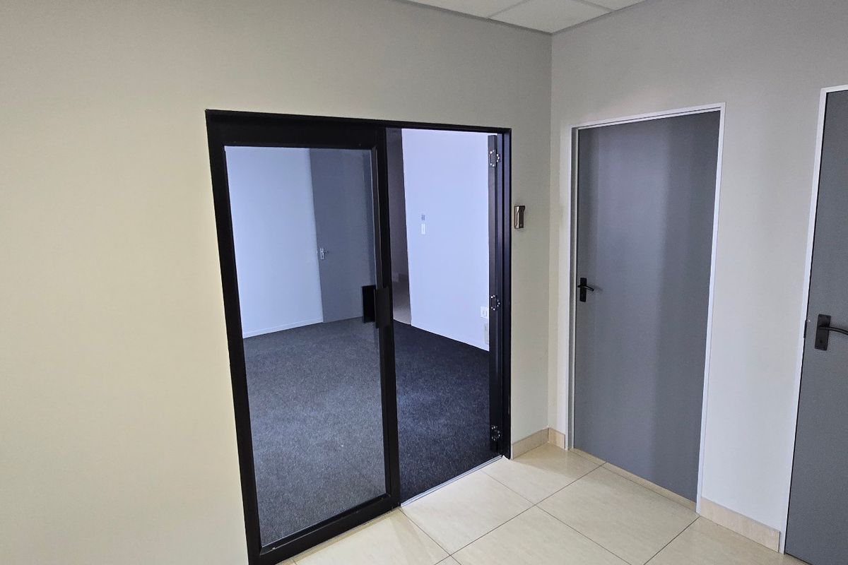 A clean, modern commercial hallway featuring tiled flooring, internal doors, and a glass sliding door leading into an office space.