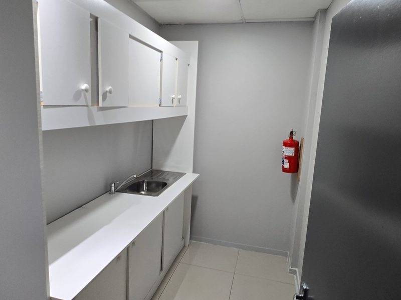 A functional kitchenette or scullery area featuring built-in cabinetry, a stainless steel sink, and tiled flooring, suitable for office or commercial utility use.