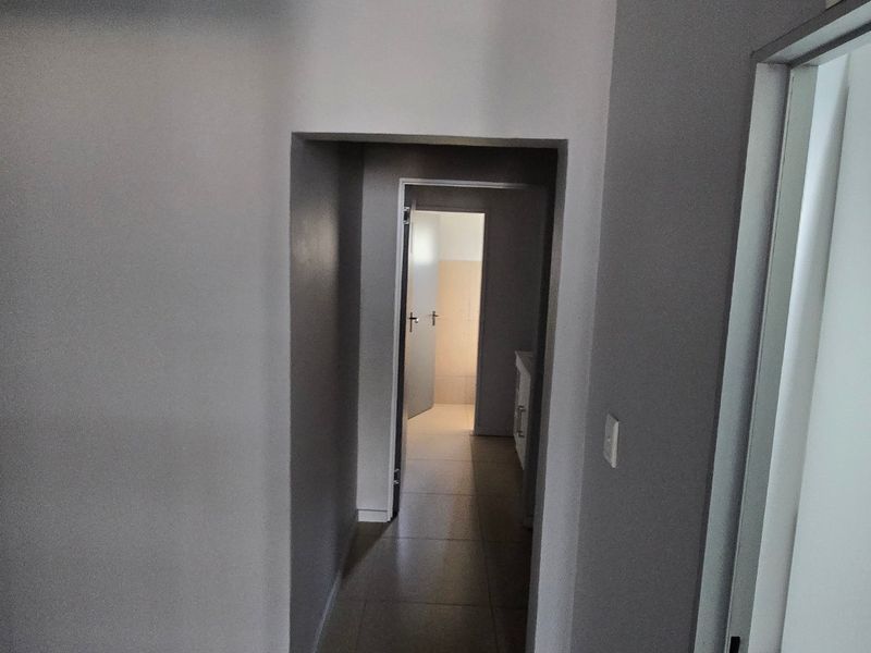 A clean, neutral-toned hallway connecting multiple interior spaces, featuring tiled flooring and standard internal door frames.