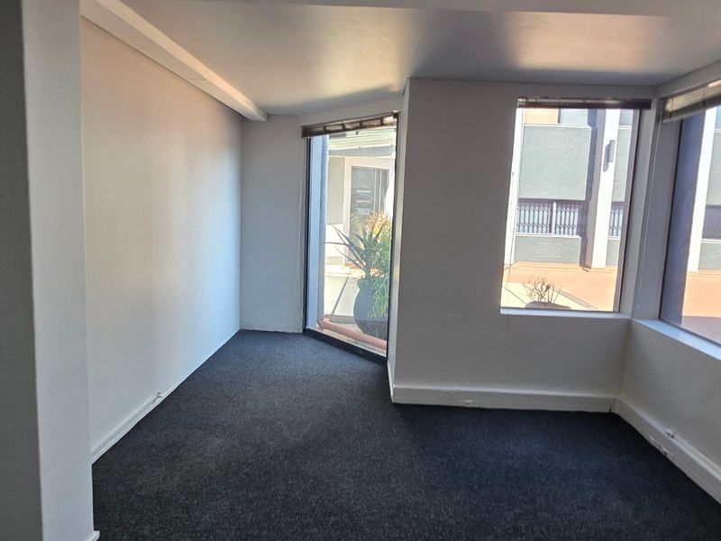 A bright, empty office space featuring dark carpeting and large windows providing natural light and views of the exterior.