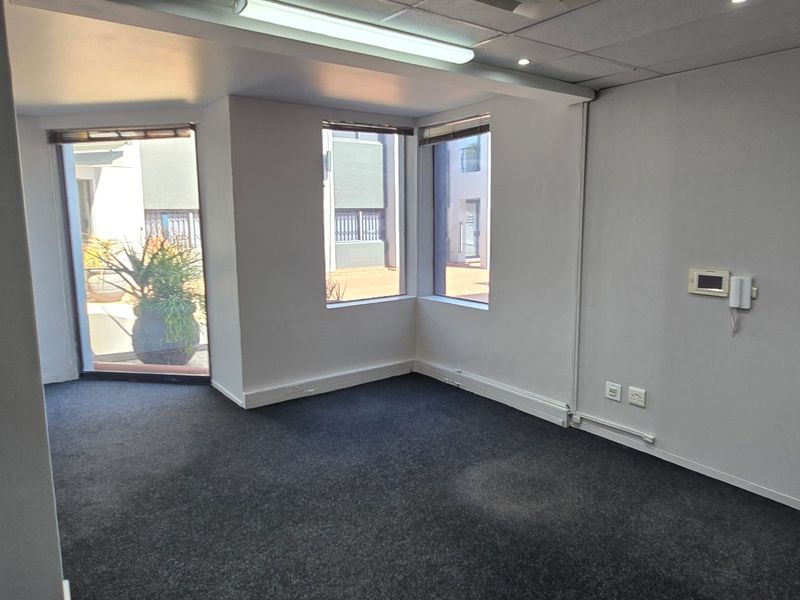 A vacant commercial office space featuring dark carpeting, suspended ceilings with integrated lighting, and an intercom system, offering a clean and functional workspace.