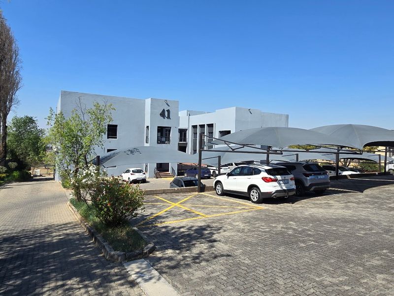 Commercial property exterior featuring a paved parking area with shade cloth carports and a modern multi-story office building facade.