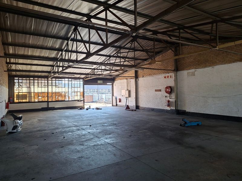 Spacious industrial utility area featuring exposed steel roof trusses, concrete flooring, and large steel-framed windows, suitable for workshop or storage use.