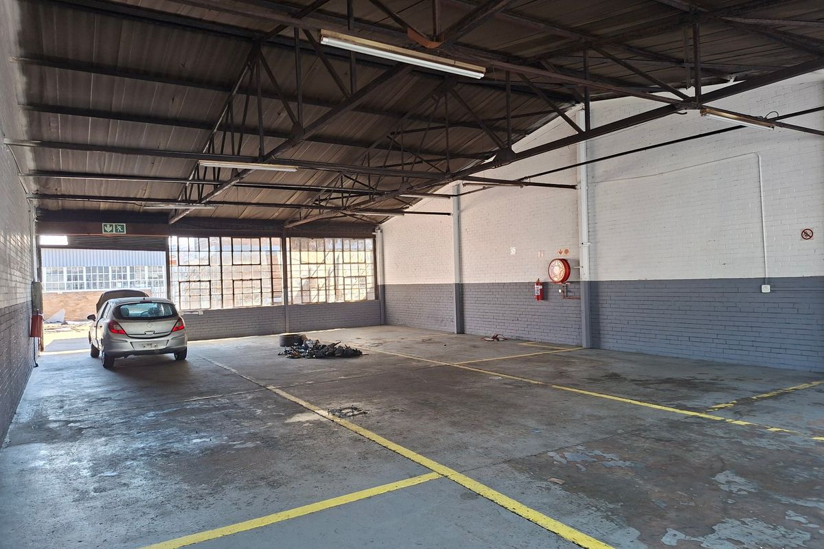 Spacious industrial garage or warehouse area featuring exposed steel roof trusses, concrete flooring, and large steel-framed windows, suitable for storage or workshop use.