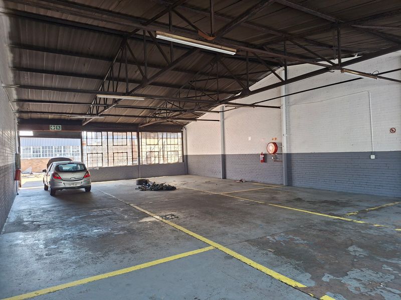 Spacious industrial garage or warehouse area featuring exposed steel roof trusses, concrete flooring, and large steel-framed windows, suitable for storage or workshop use.