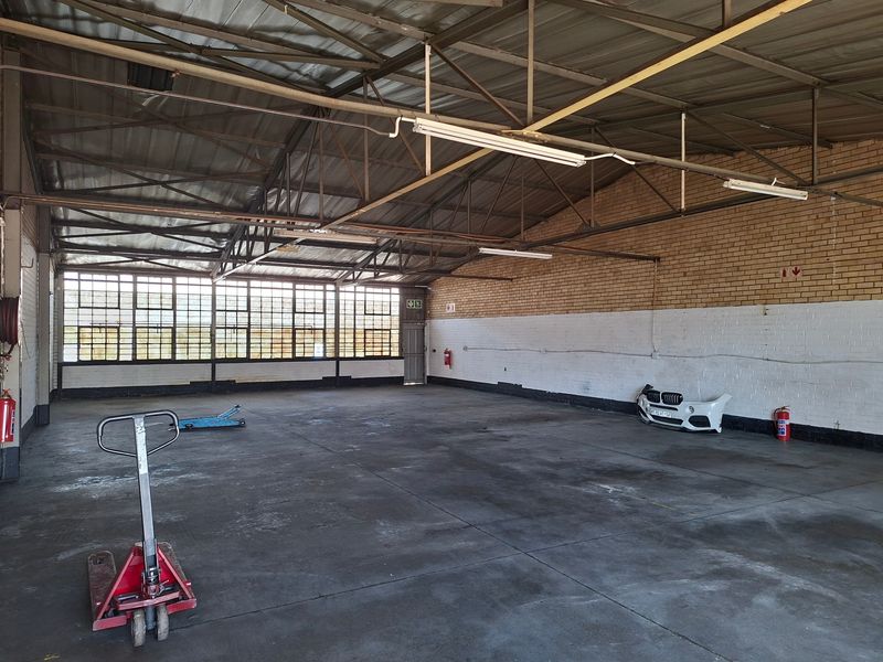 Spacious industrial warehouse unit featuring high ceilings with exposed steel trusses, large windows for natural light, and durable concrete flooring.