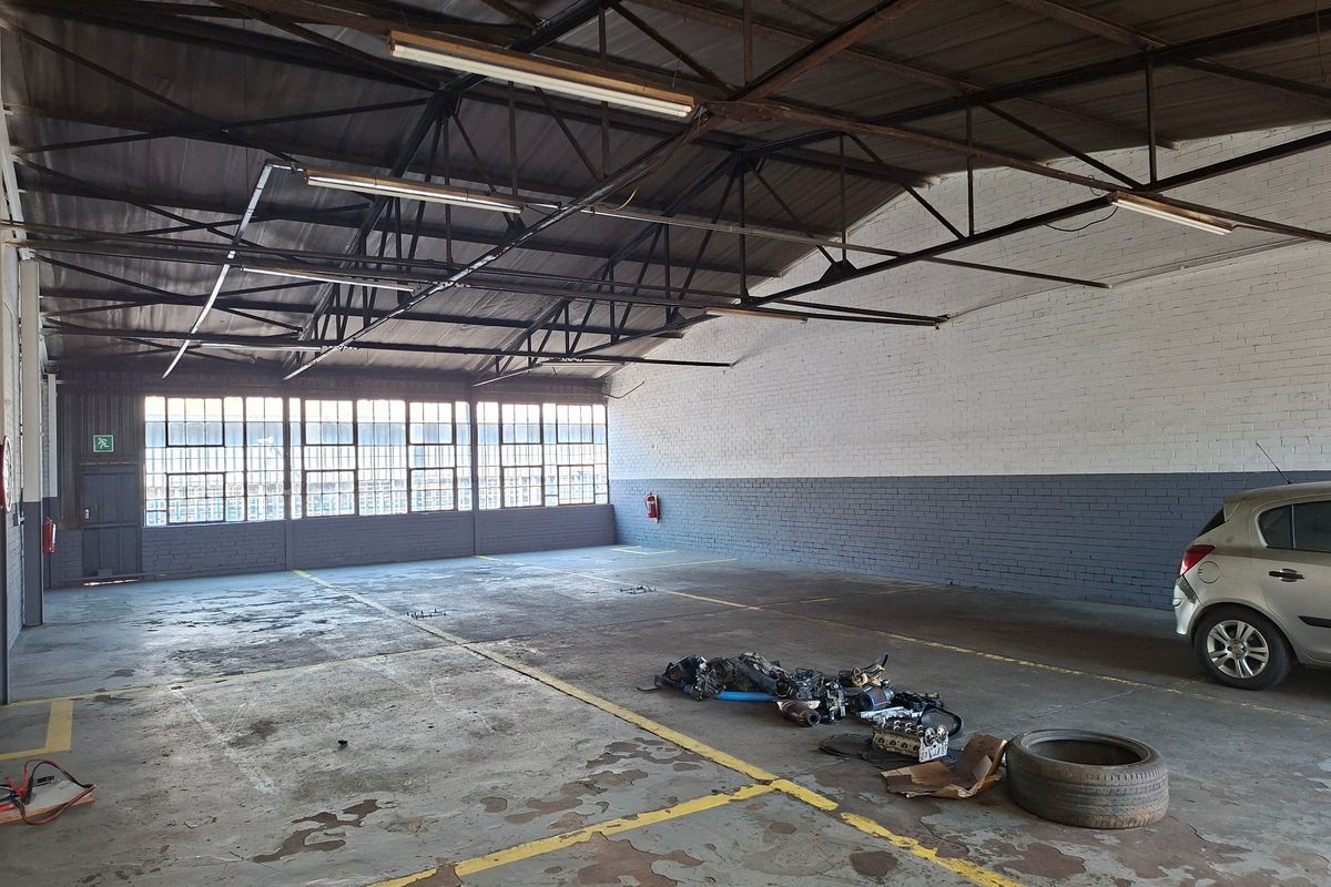 Spacious industrial garage featuring exposed steel roof trusses, large steel-framed windows, and durable concrete flooring, suitable for workshop or storage use.
