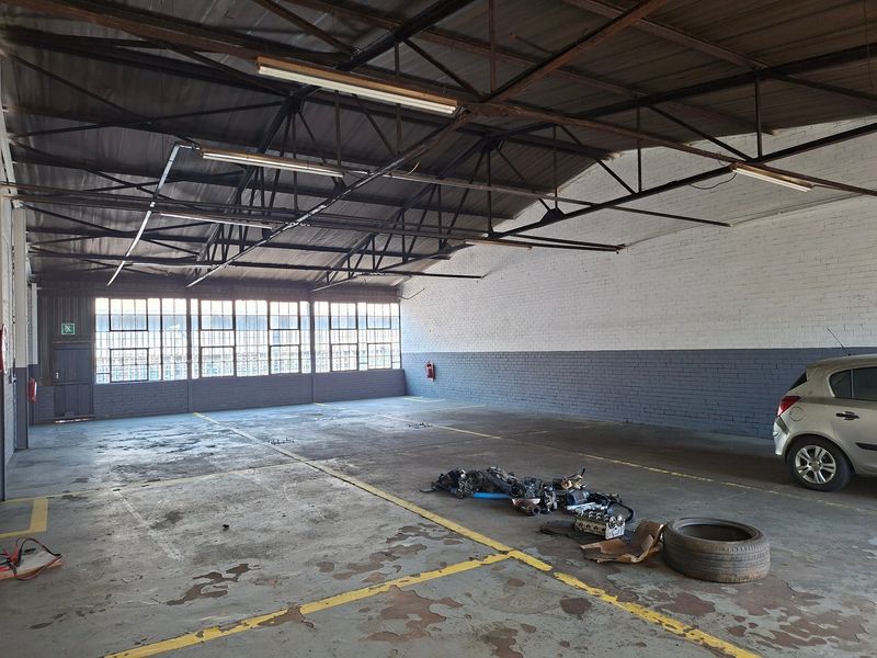 Spacious industrial garage featuring exposed steel roof trusses, large steel-framed windows, and durable concrete flooring, suitable for workshop or storage use.