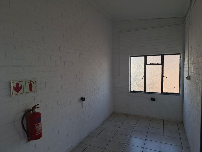 A clean, empty industrial office space featuring white-painted brick walls, tiled flooring, and a steel-framed window with natural light.