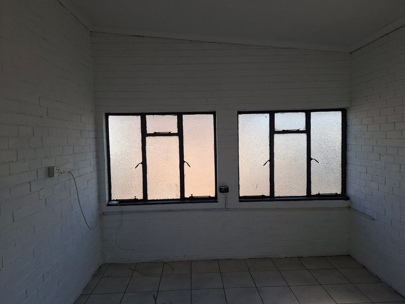 An empty utility space featuring painted brick walls, tiled flooring, and two steel-framed windows with textured glass.