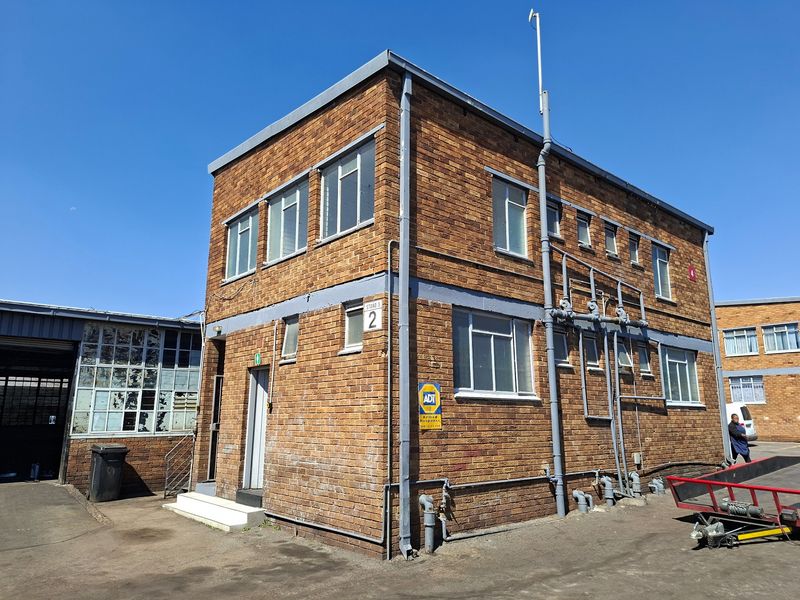 A two-story industrial building featuring a face brick facade, external plumbing infrastructure, and aluminium window frames, situated in an industrial complex.