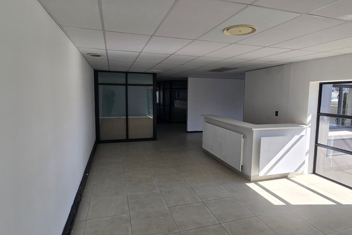A bright, open-plan office space featuring tiled flooring, a built-in reception desk, and modern glass partitioning, suitable for a professional commercial environment.
