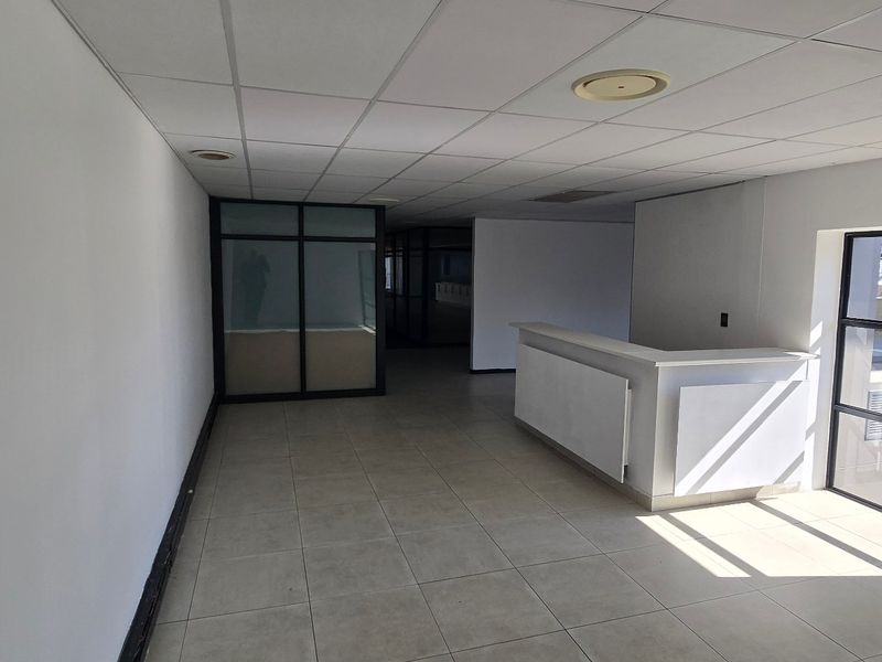 A bright, open-plan office space featuring tiled flooring, a built-in reception desk, and modern glass partitioning, suitable for a professional commercial environment.