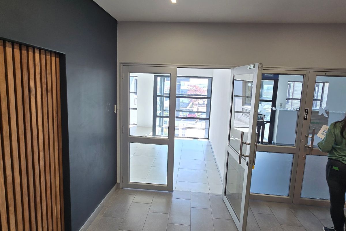 Modern commercial entrance foyer featuring timber slat wall detailing, tiled flooring, and aluminium framed glass doors leading to an open office space.