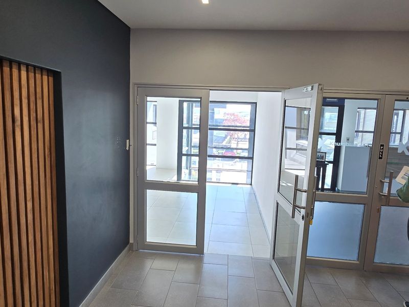 Modern commercial entrance foyer featuring timber slat wall detailing, tiled flooring, and aluminium framed glass doors leading to an open office space.