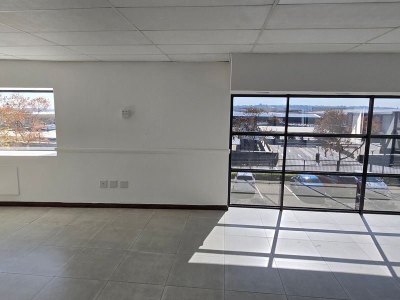 A bright, empty commercial office space featuring large windows, tiled flooring, and a suspended ceiling, offering ample natural light and a professional layout.