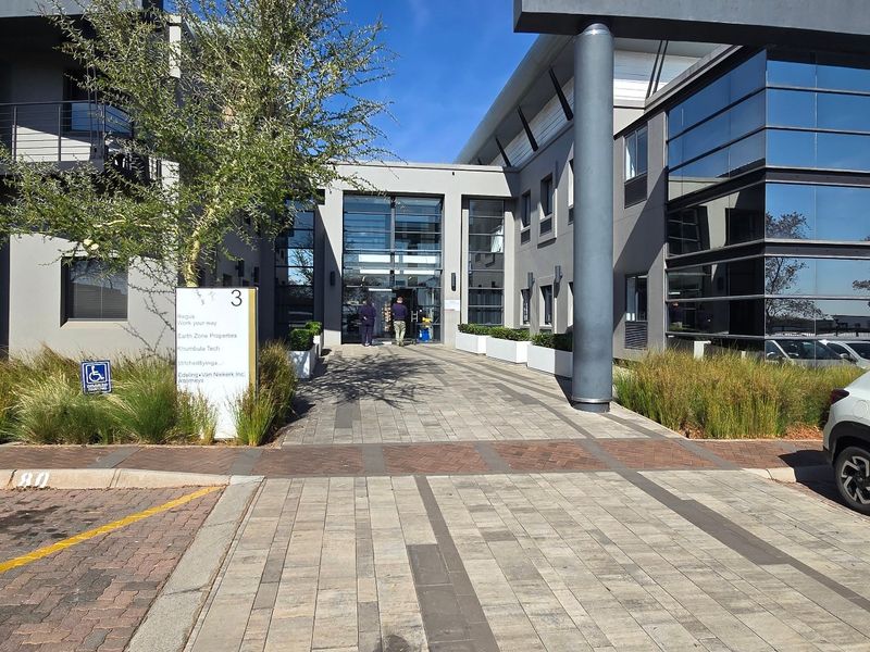 Modern commercial office building entrance featuring a paved walkway, glass facade, and professional signage in a well-maintained business park setting.